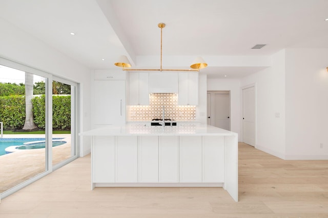 kitchen featuring light countertops, light wood-style flooring, backsplash, a kitchen island with sink, and white cabinets