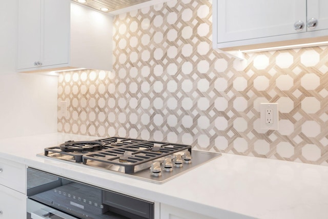 kitchen with light countertops, white cabinets, stainless steel gas stovetop, and backsplash