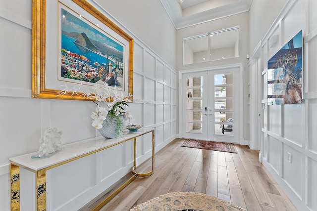 entrance foyer featuring light wood-style floors, a decorative wall, crown molding, and french doors