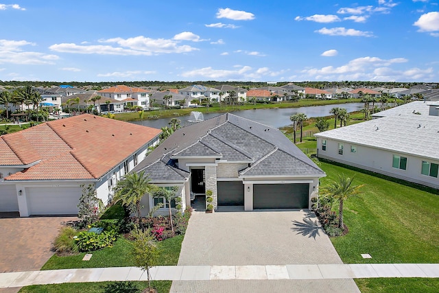 view of front of home featuring decorative driveway, a water view, a front yard, a garage, and a residential view