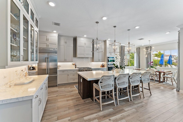 kitchen with tasteful backsplash, a center island with sink, visible vents, light wood-style flooring, and appliances with stainless steel finishes