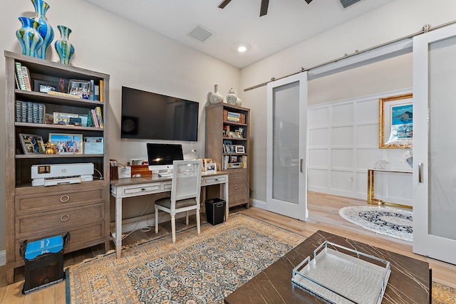 office area featuring ceiling fan, a barn door, wood finished floors, visible vents, and french doors