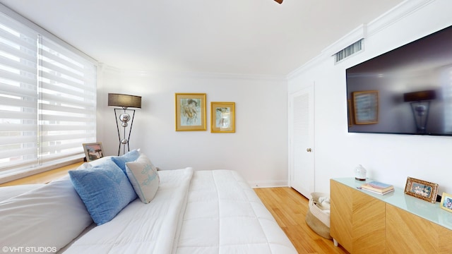 bedroom with baseboards, wood finished floors, visible vents, and crown molding