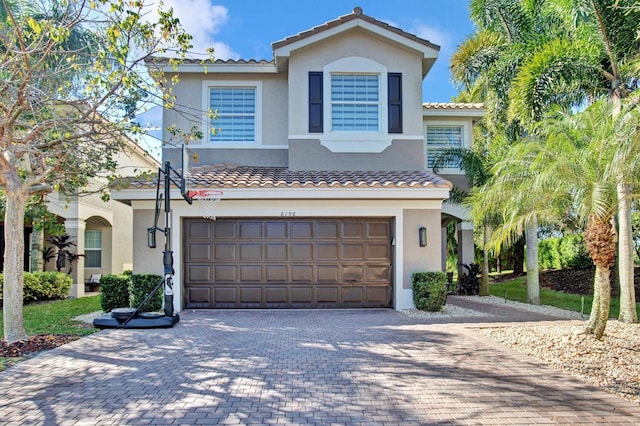 mediterranean / spanish-style home featuring stucco siding, decorative driveway, an attached garage, and a tiled roof