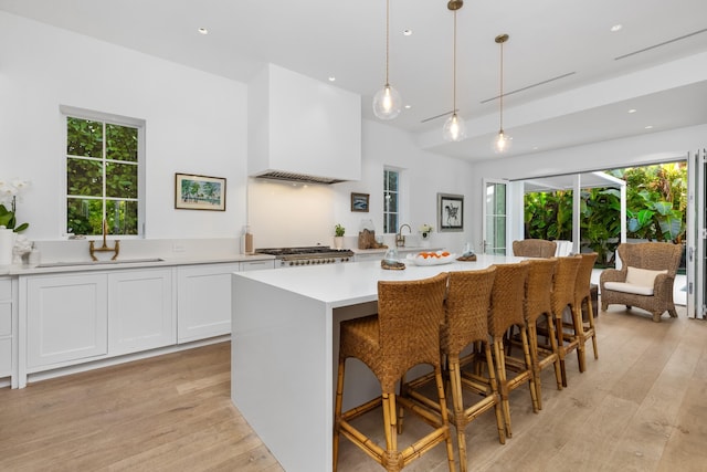 kitchen with premium range hood, a sink, white cabinets, light wood-style floors, and light countertops