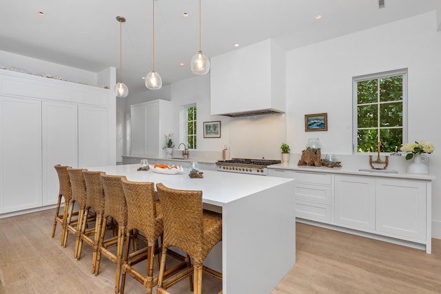 kitchen with white cabinetry, light countertops, range, a center island, and custom range hood