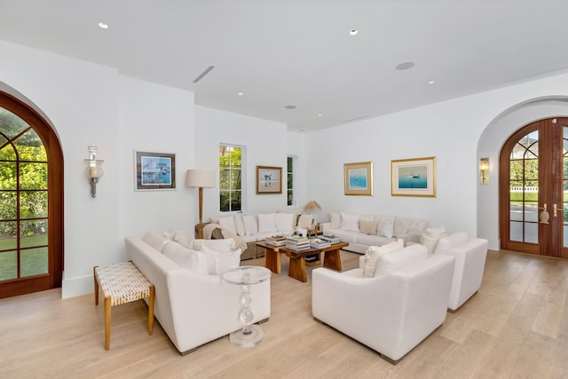 living room with arched walkways, french doors, light wood finished floors, and plenty of natural light