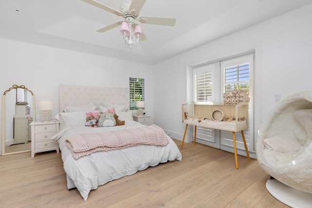 bedroom featuring light wood-style floors, baseboards, a tray ceiling, and a ceiling fan