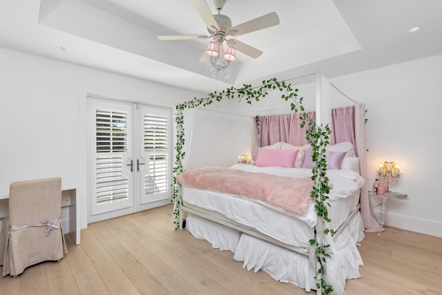 bedroom with ceiling fan, light wood finished floors, a raised ceiling, and access to exterior