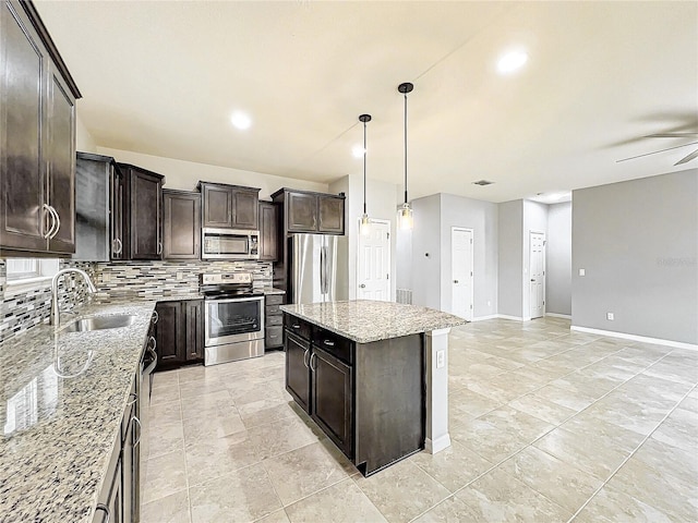 kitchen with a sink, hanging light fixtures, appliances with stainless steel finishes, a center island, and tasteful backsplash