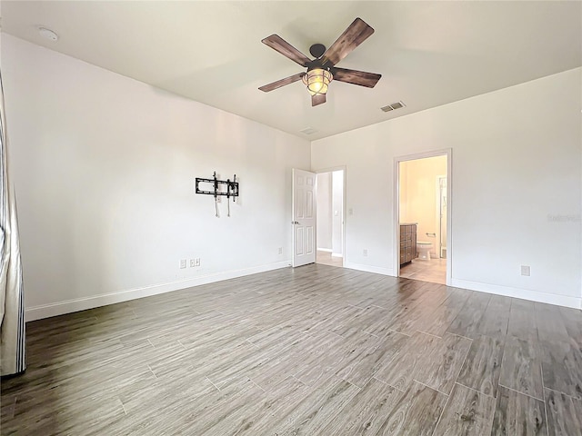 unfurnished bedroom featuring ensuite bathroom, wood finished floors, a ceiling fan, visible vents, and baseboards