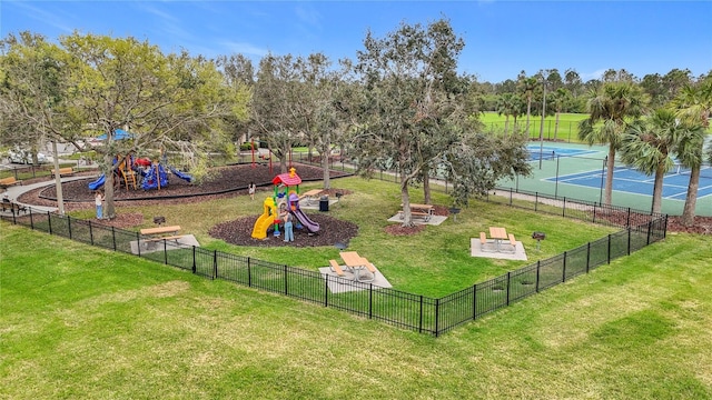 view of property's community with a yard, playground community, a tennis court, and fence