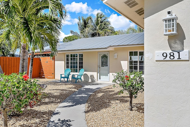 property entrance featuring metal roof, fence, a standing seam roof, and stucco siding