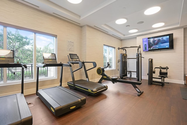 exercise room with a raised ceiling, dark wood finished floors, and baseboards