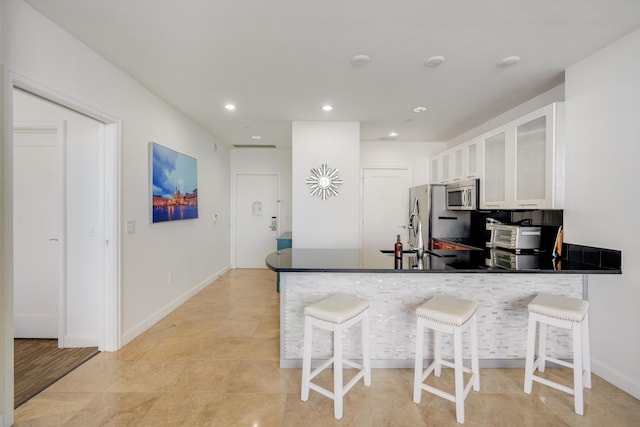 kitchen featuring appliances with stainless steel finishes, a kitchen breakfast bar, glass insert cabinets, a peninsula, and white cabinetry