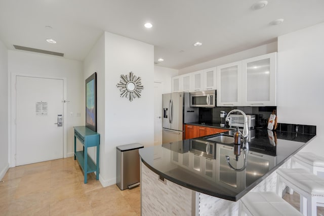 kitchen featuring dark countertops, appliances with stainless steel finishes, backsplash, a breakfast bar area, and a sink