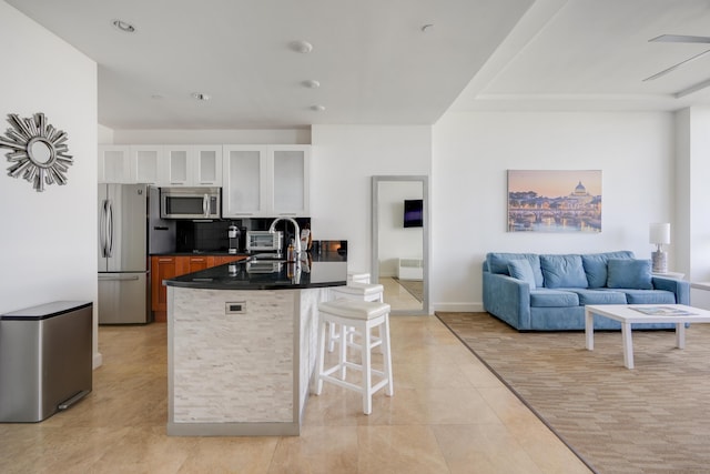 kitchen featuring stainless steel appliances, a sink, dark countertops, a kitchen bar, and glass insert cabinets