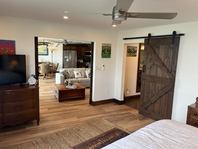 bedroom with a barn door, stainless steel refrigerator with ice dispenser, recessed lighting, and light wood-style floors