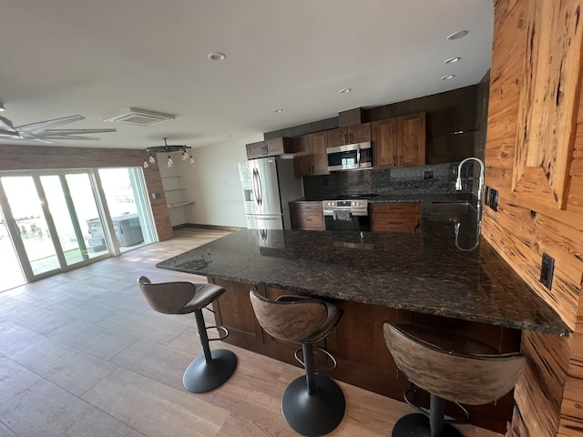 kitchen featuring a breakfast bar area, stainless steel appliances, a peninsula, decorative backsplash, and dark stone counters