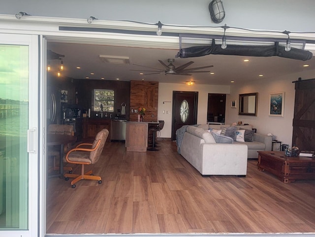 living room featuring ceiling fan, a barn door, and wood finished floors