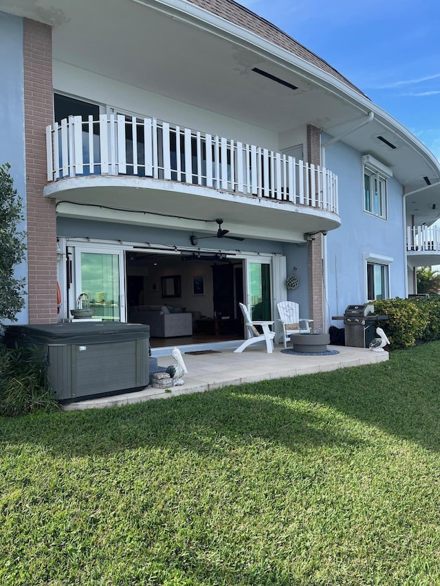 back of house featuring a patio, a balcony, a lawn, stucco siding, and a hot tub