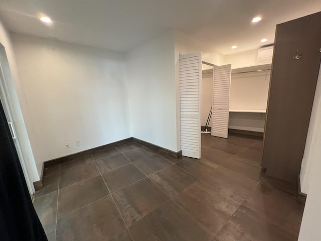 interior space with baseboards, dark tile patterned flooring, a spacious closet, an AC wall unit, and recessed lighting