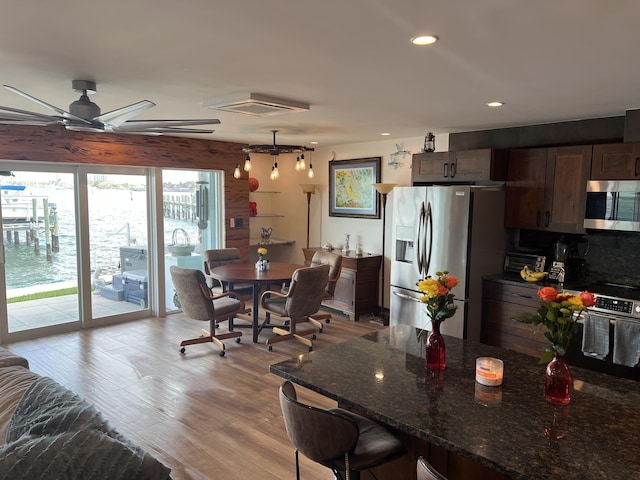 kitchen featuring dark stone counters, light wood-style flooring, stainless steel appliances, a kitchen bar, and recessed lighting