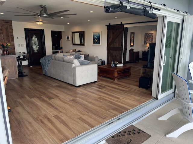 living area with light wood-type flooring, ceiling fan, recessed lighting, and a barn door