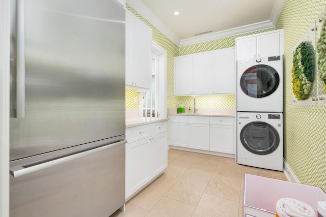 kitchen with wallpapered walls, stacked washer and dryer, white cabinets, stainless steel refrigerator, and light countertops