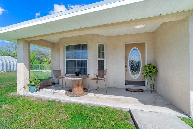 doorway to property with a patio, a lawn, fence, and stucco siding