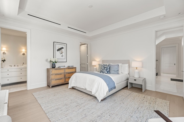 bedroom featuring wood finished floors, ensuite bath, and a raised ceiling