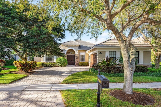 view of front of home with decorative driveway, stone siding, a tiled roof, and stucco siding