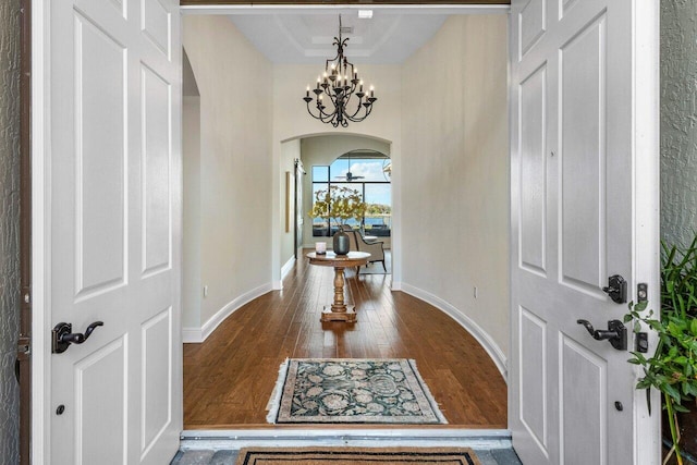 entryway with arched walkways, a chandelier, baseboards, dark wood-style floors, and a tray ceiling