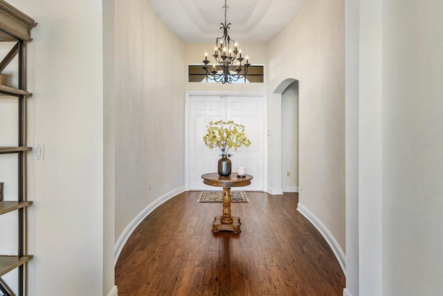 dining room with dark wood-style floors, arched walkways, a raised ceiling, a chandelier, and baseboards