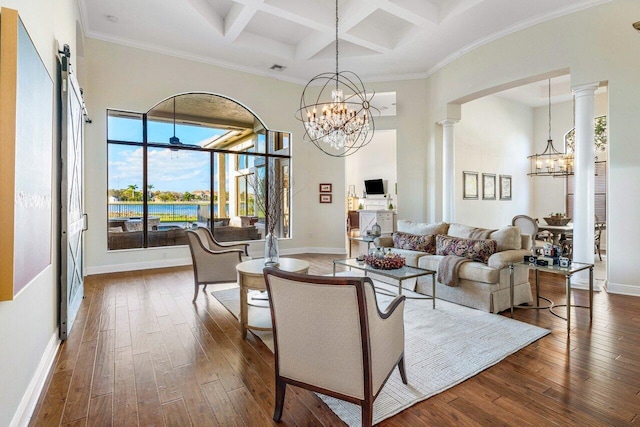 living room featuring a towering ceiling, ornate columns, a chandelier, and dark wood-style flooring