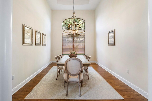 dining area featuring dark wood-style floors, a raised ceiling, a notable chandelier, and baseboards