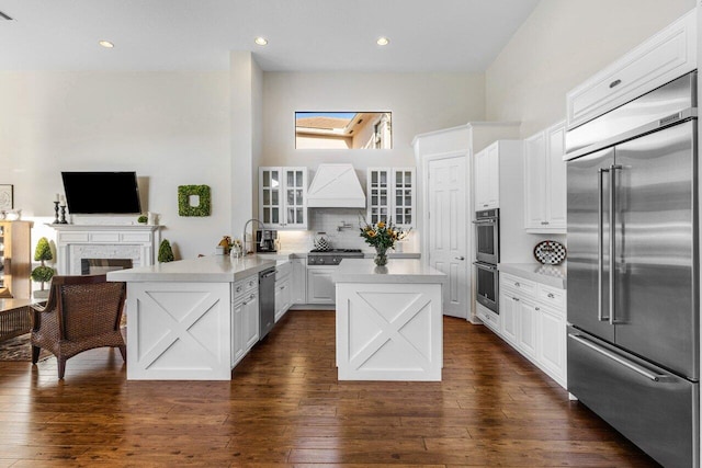 kitchen featuring dark wood finished floors, light countertops, appliances with stainless steel finishes, premium range hood, and a peninsula