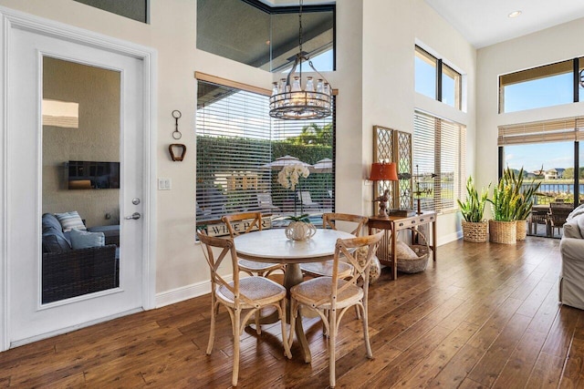 dining space with baseboards, dark wood finished floors, a towering ceiling, a notable chandelier, and recessed lighting