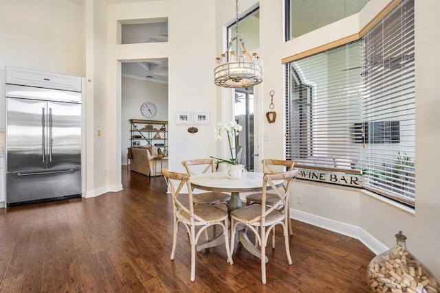 dining space with a chandelier, a high ceiling, dark wood finished floors, and baseboards