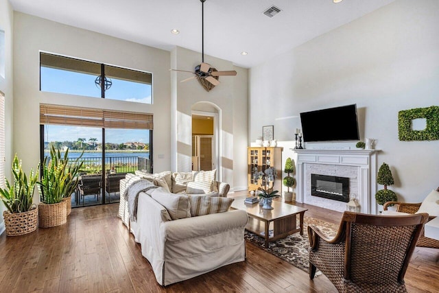 living room with visible vents, a high ceiling, a ceiling fan, a glass covered fireplace, and hardwood / wood-style floors