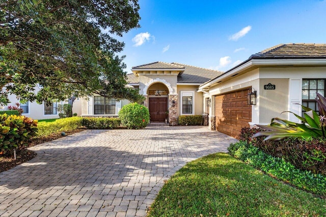 mediterranean / spanish-style house featuring a tiled roof, decorative driveway, an attached garage, and stucco siding