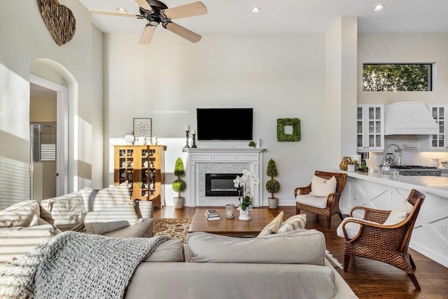 living area featuring recessed lighting, a high ceiling, a glass covered fireplace, ceiling fan, and wood finished floors