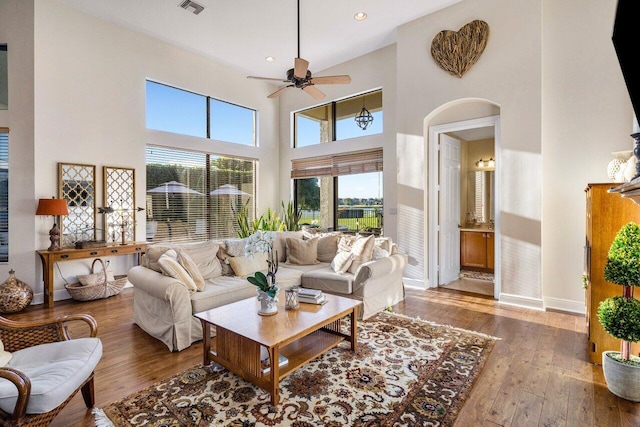 living area with arched walkways, visible vents, a towering ceiling, hardwood / wood-style floors, and baseboards