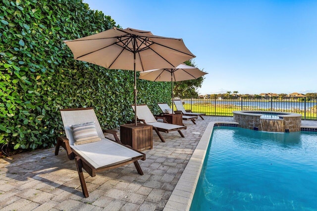 view of swimming pool featuring a water view, a patio area, a pool with connected hot tub, and fence