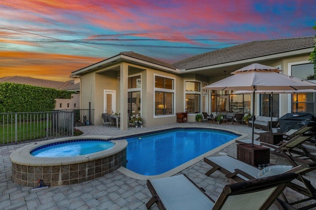 pool at dusk featuring a pool with connected hot tub, fence, grilling area, and a patio