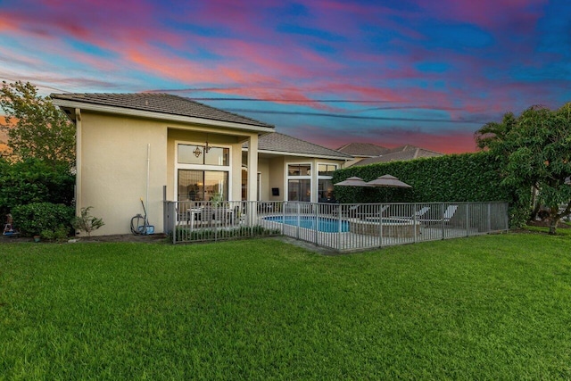 back of house at dusk with a fenced in pool, a lawn, fence, and stucco siding