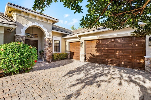 view of front of property featuring an attached garage, stone siding, decorative driveway, and stucco siding