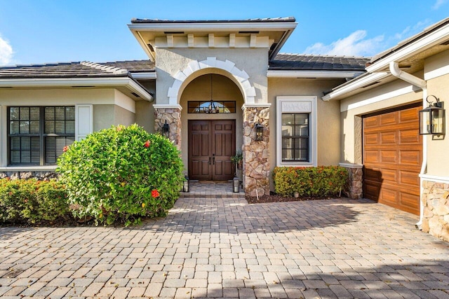 entrance to property featuring a garage, stone siding, and stucco siding