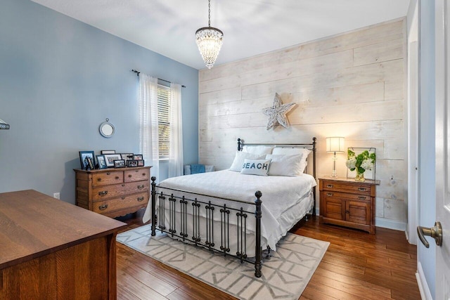 bedroom featuring a chandelier, wooden walls, wood-type flooring, and baseboards