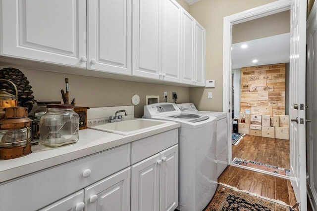 laundry room featuring cabinet space, wood finished floors, washing machine and dryer, a sink, and recessed lighting